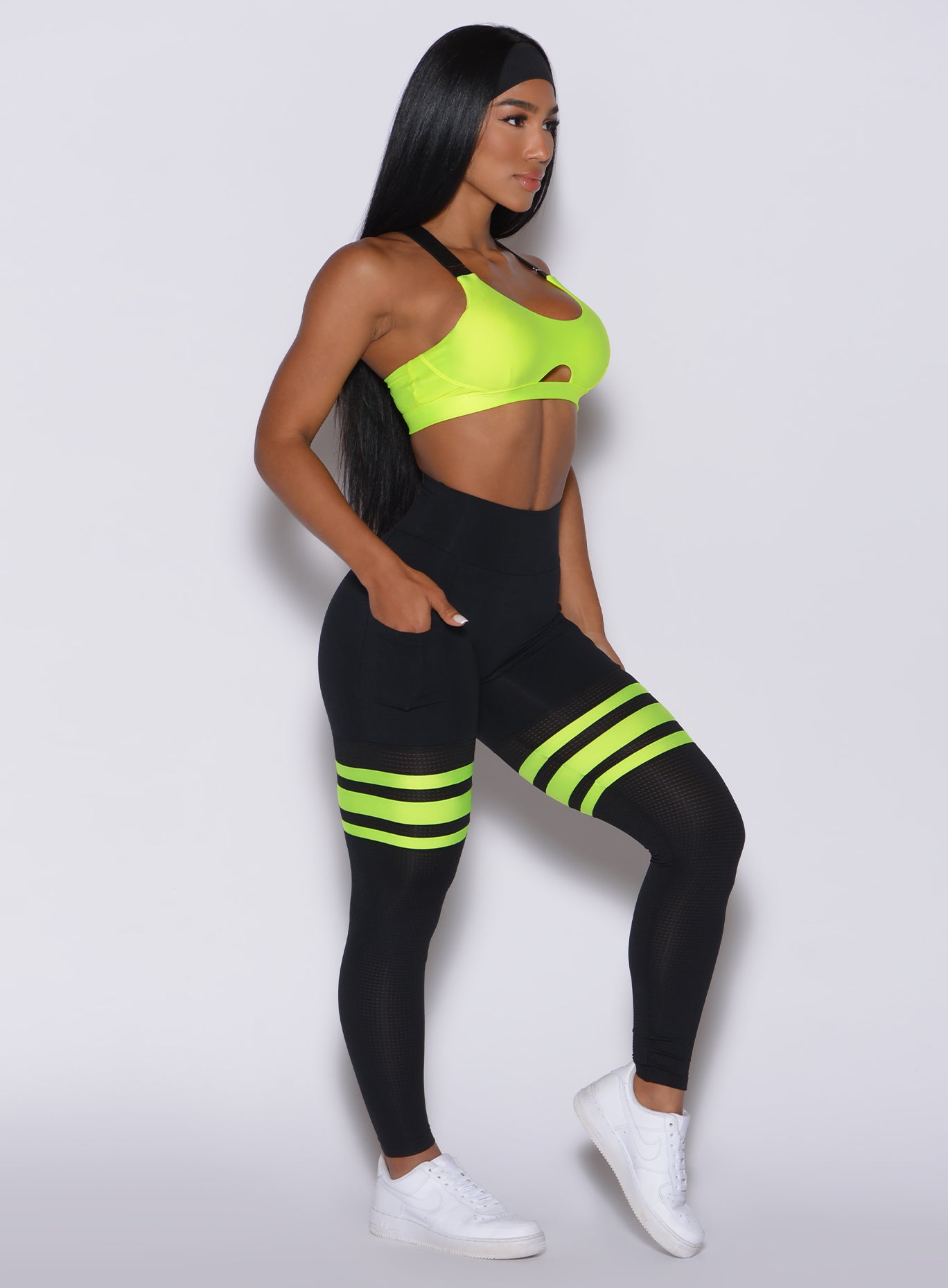 Right side profile view of a model wearing our scrunch thigh high in black with neon yellow stripes on the thighs and a matching sports bra