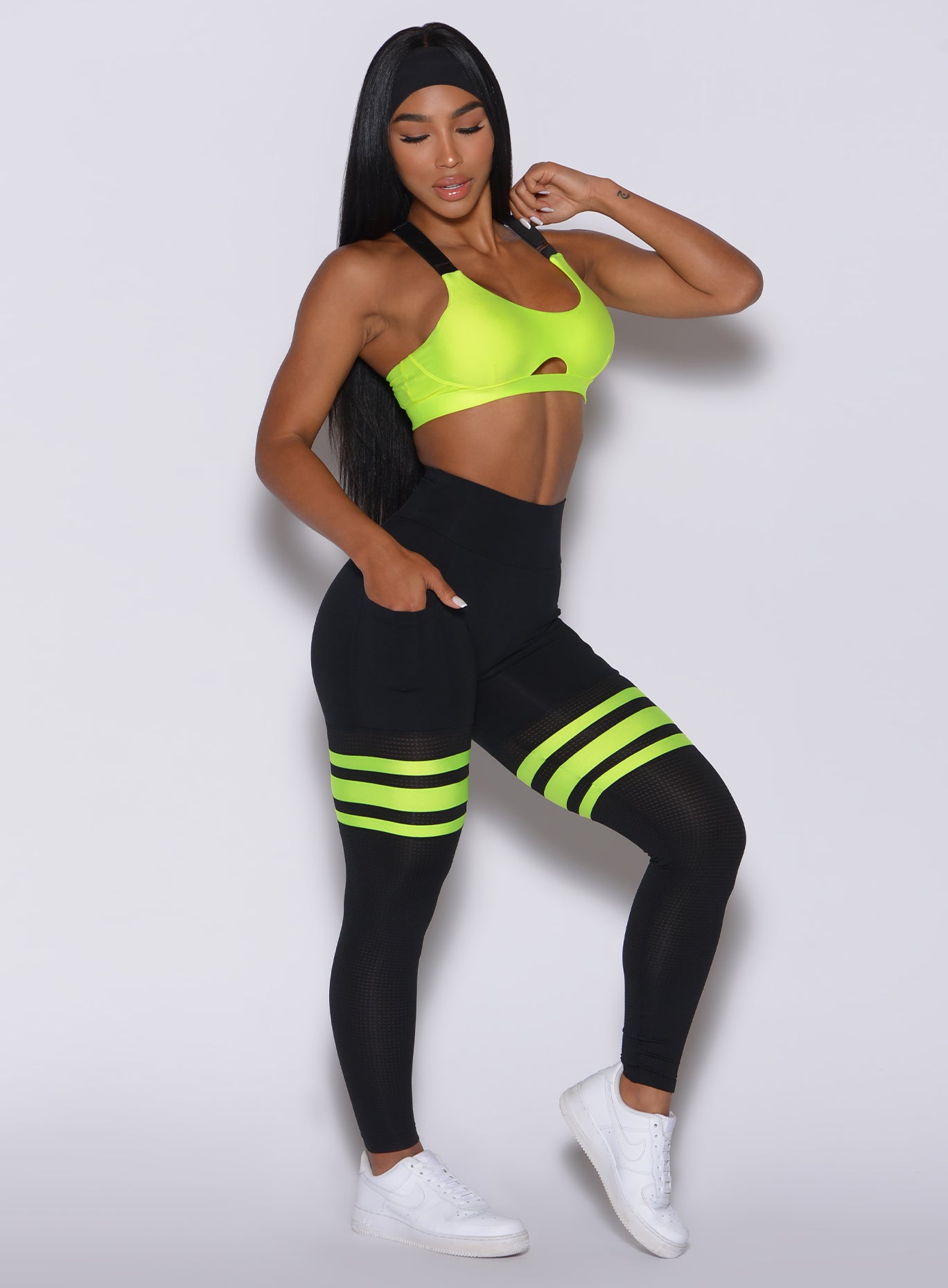 Right side profile view of a model looking at the floor wearing our scrunch thigh high in black with neon yellow stripes on the thighs and a matching sports bra