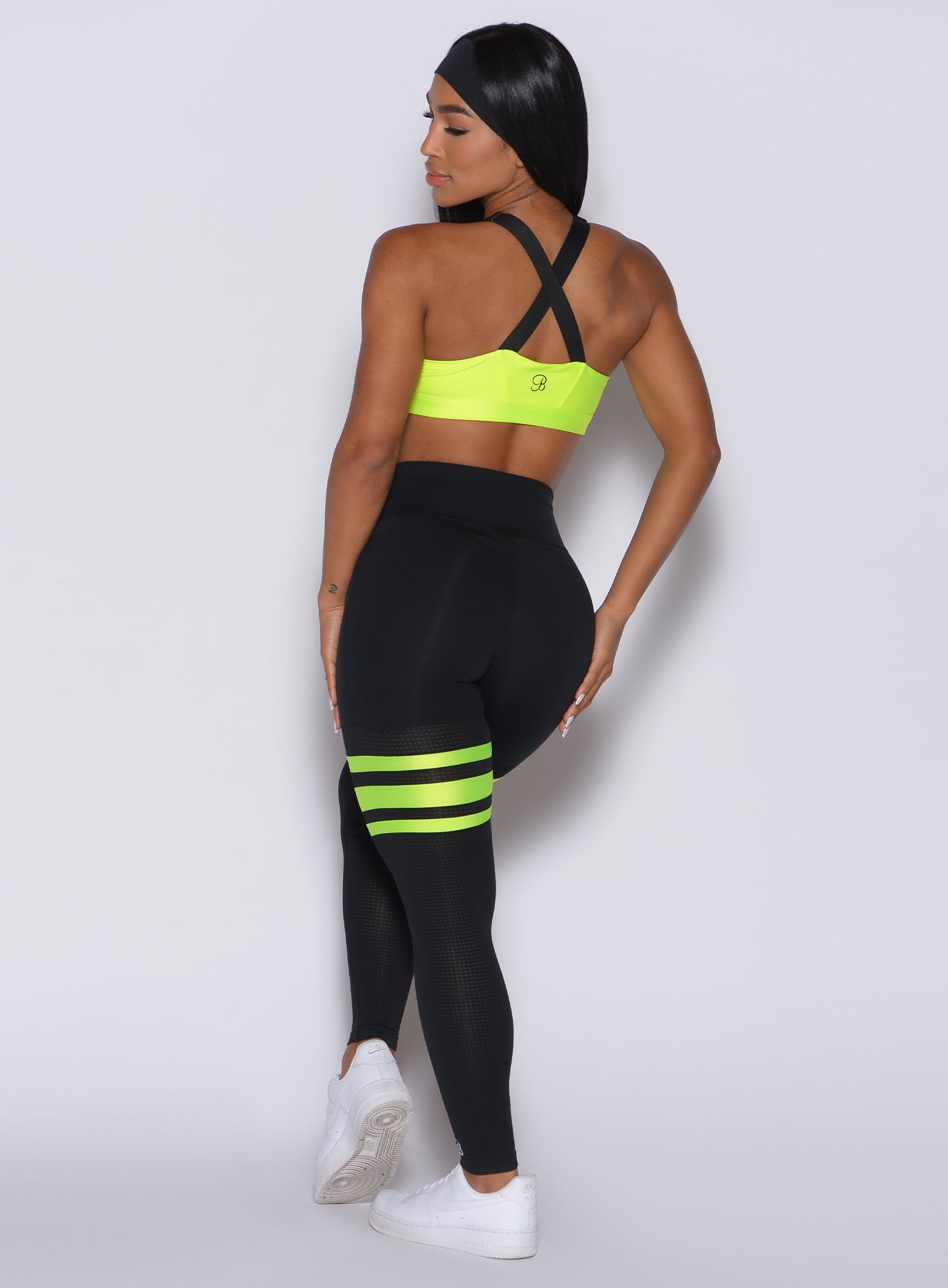 Back profile view of a model in our scrunch thigh high in black with neon yellow stripes on the thighs and a matching sports bra