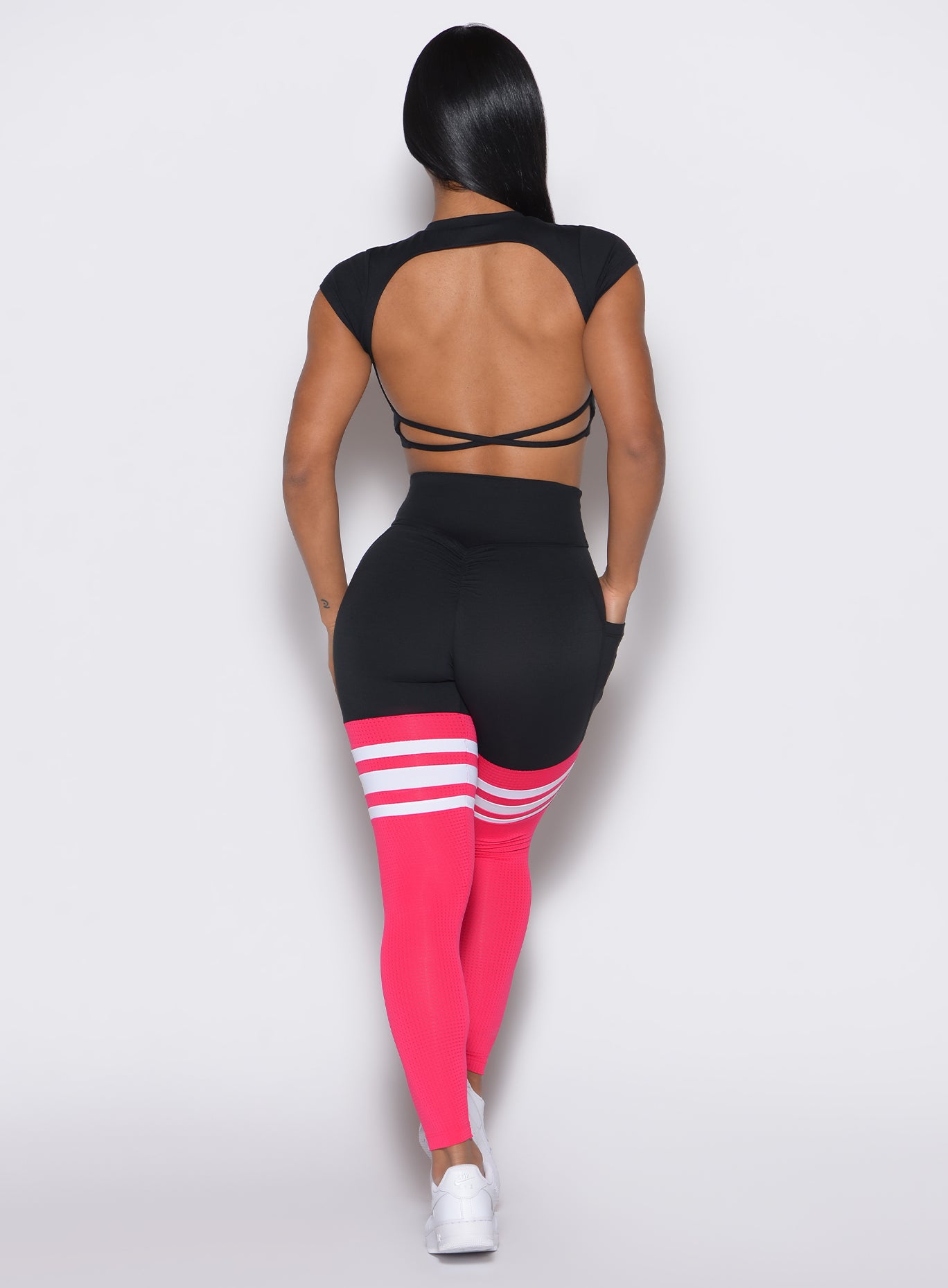 Back profile view of a model wearing the Scrunch Thigh Highs in Black and Berry Color along with a black tee