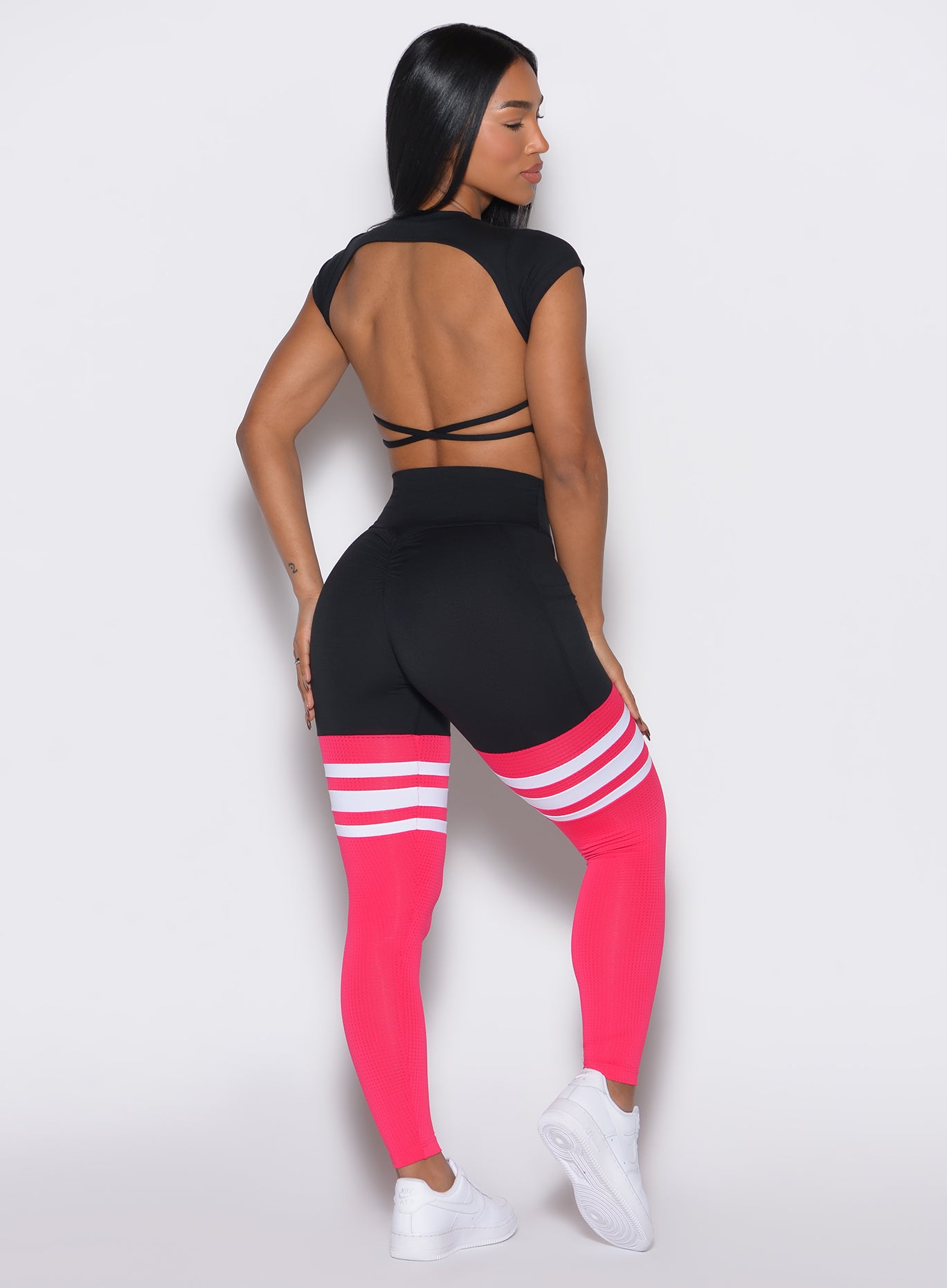 Back profile view of a model facing right wearing the Scrunch Thigh Highs in Black and Berry Color along with a black tee