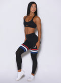 Three quarters view of the model wearing our Scrunch Thigh high in black with three stripes on the thighs and a black sports bra