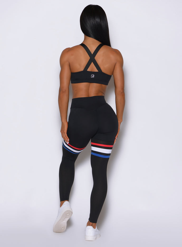 Back view of the model wearing our Scrunch Thigh high in black with three stripes on the thighs and a black sports bra