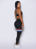 Right side view of the model wearing our high waisted Scrunch Thigh high in black with three stripes on the thighs and a black sports bra