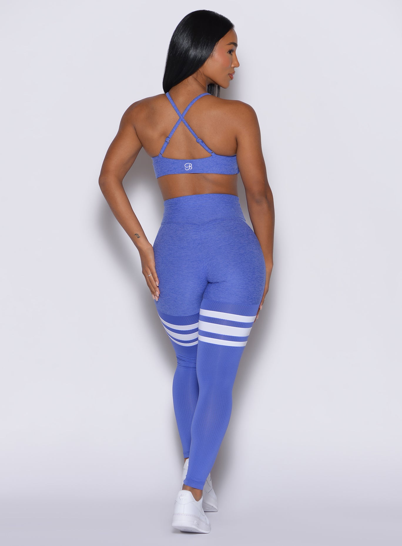 Back profile view of a model wearing our scrunch thigh-highs in violet blue with three white stripes on the thighs, complemented by a matching sports bra.