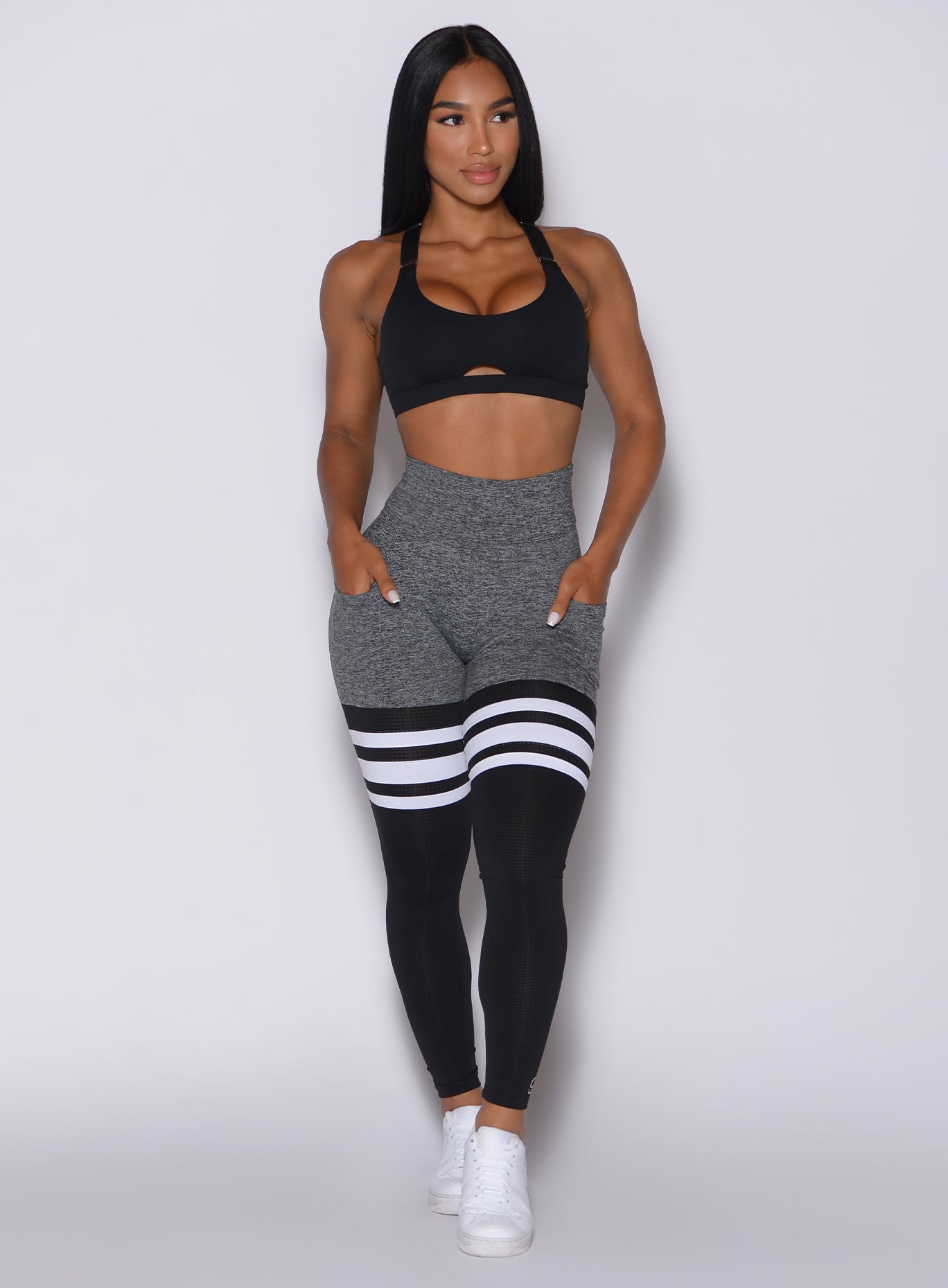 Front profile view of a model in our scrunch thigh high in gray and black with three stripes on the thighs and a matching black bra