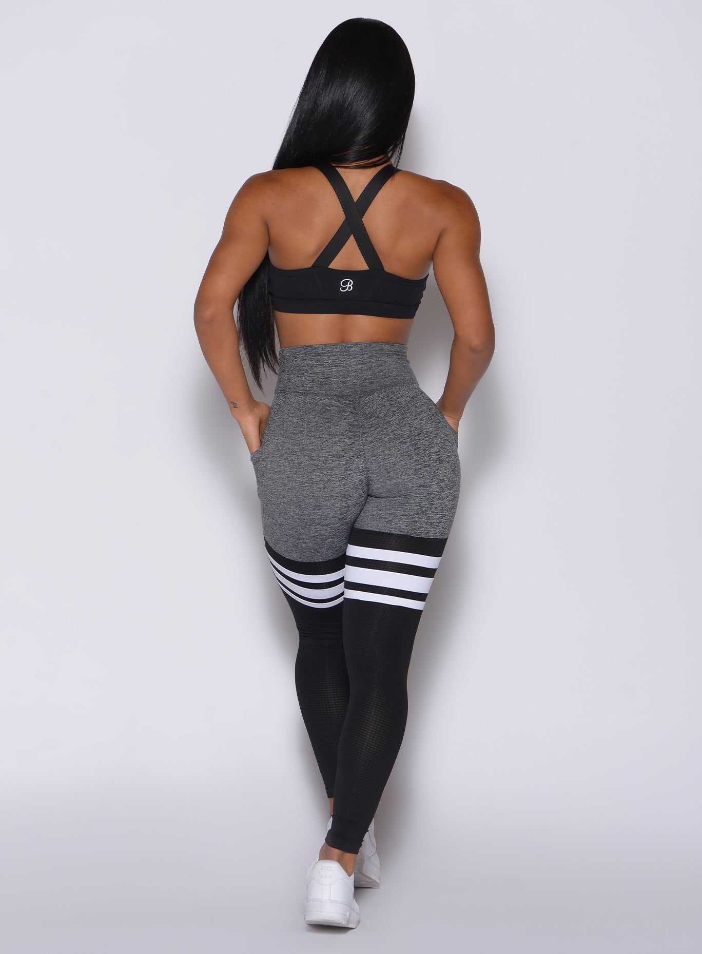 Back profile view of a model in our scrunch thigh high in gray and black with three stripes on the thighs and a matching black bra 