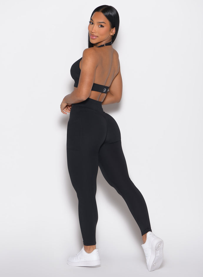 left side profile view of a model looking over her shoulder wearing the Sculpt Knot Leggings in black color