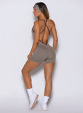 back side profile view of a model facing to the left side wearing the Lift Bodysuit Shorts in Stone color