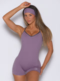 front profile view of a model with hand resting on top of her head wearing the Lift Bodysuit Shorts in Violet frost color