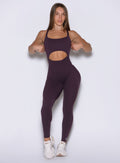 front view of a model adjusting the sides wearing the Sculptura Bodysuit in plum noir color
