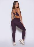 back right side profile view of a model looking over her shoulder wearing the Sculptura Bodysuit in plum noir color