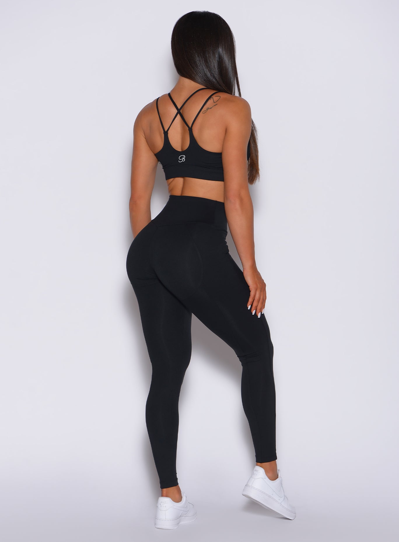 Back profile view of a model in our new and enhanced black shape leggings and a matching bra