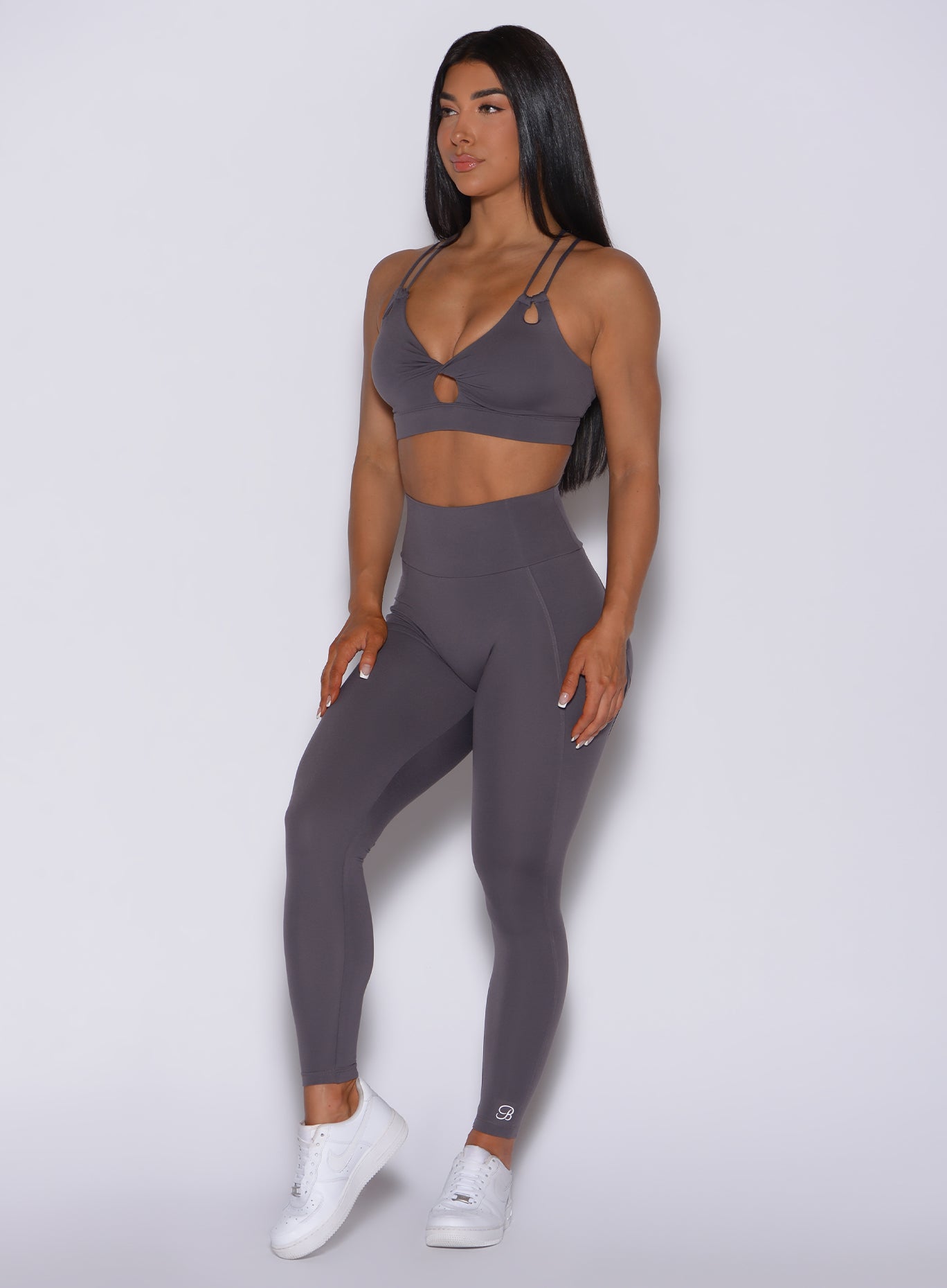 Front profile view of a model angled slightly to her right wearing our new and enhanced shape leggings in gray smoke color and a matching bra
