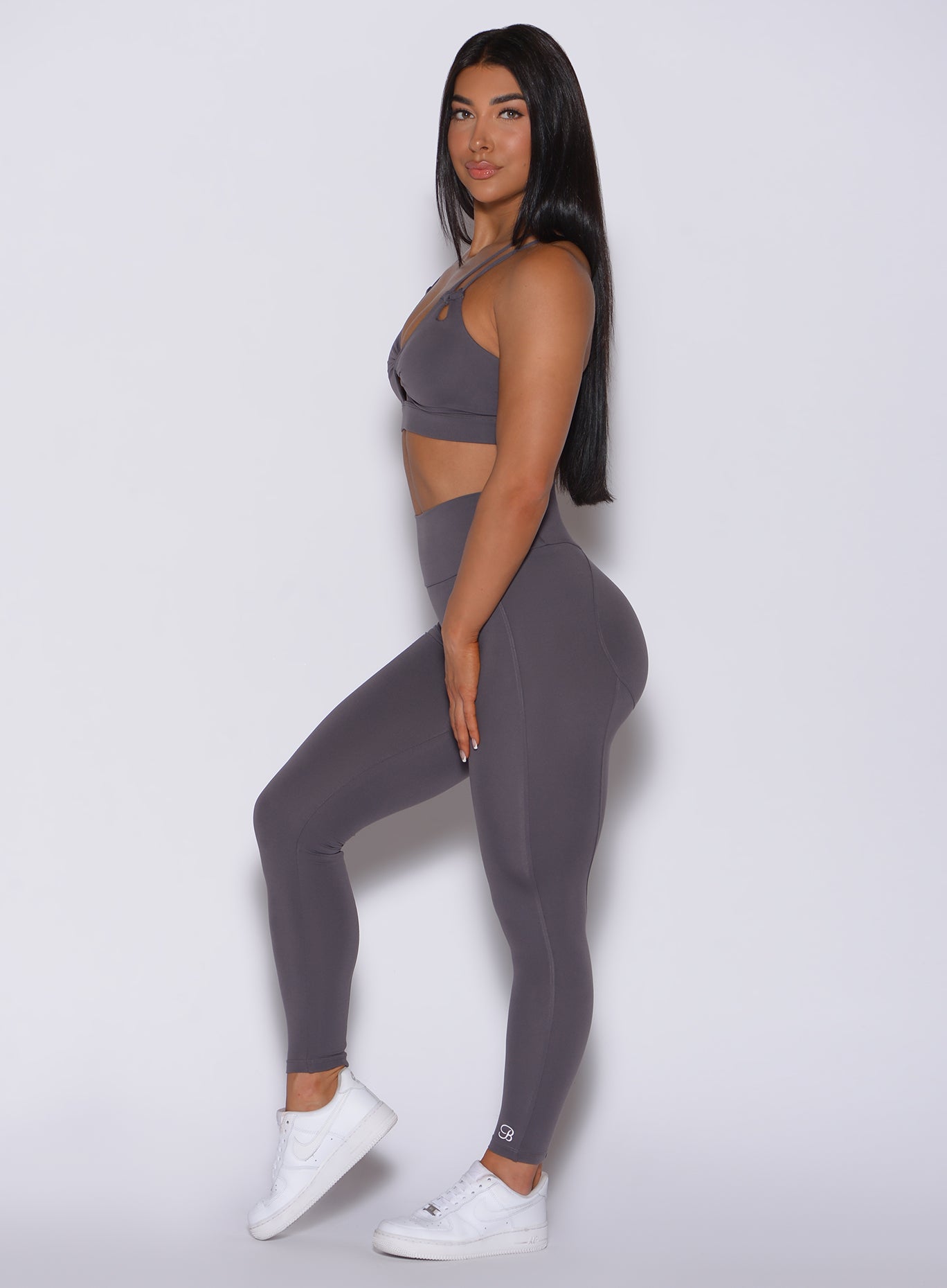 Left side profile view of a model in our new and enhanced shape leggings in gray smoke color and a matching bra