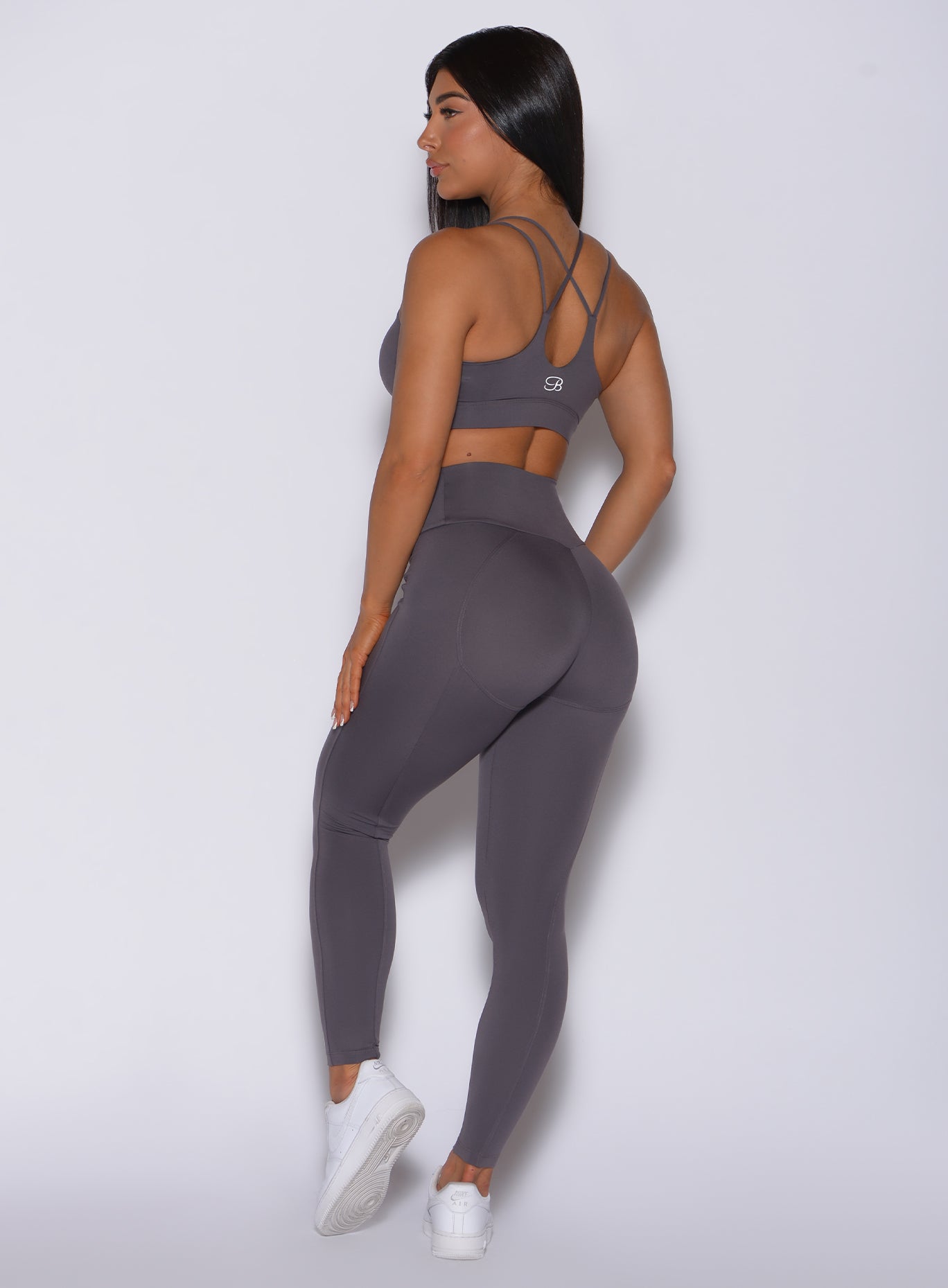 Back profile view of a model in our new and enhanced shape leggings in gray smoke color and a matching sports bra