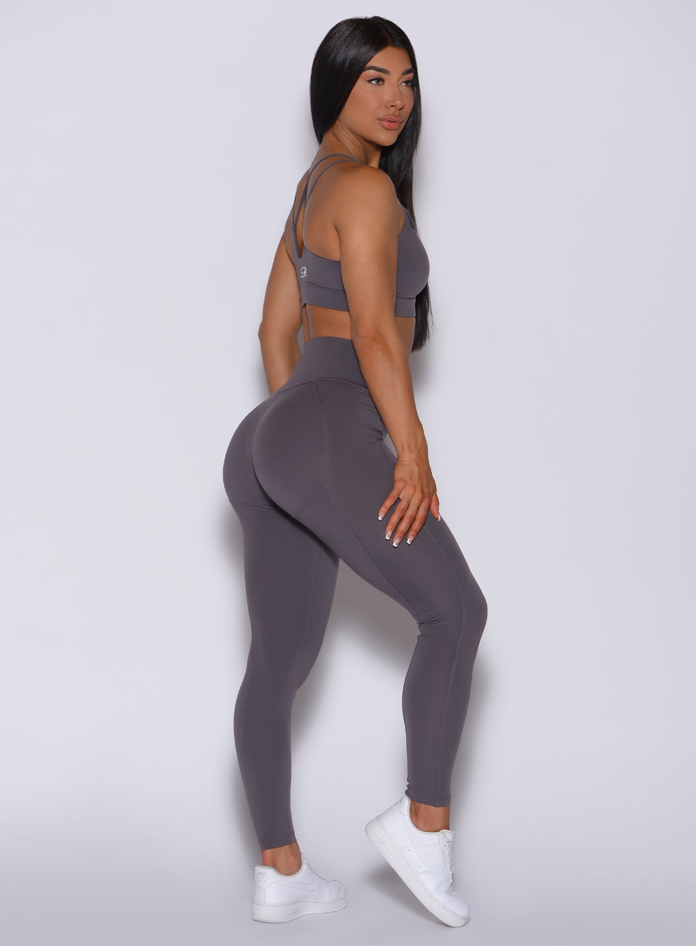 Right side profile view of a model in our new and enhanced shape leggings in gray smoke color and a matching bra