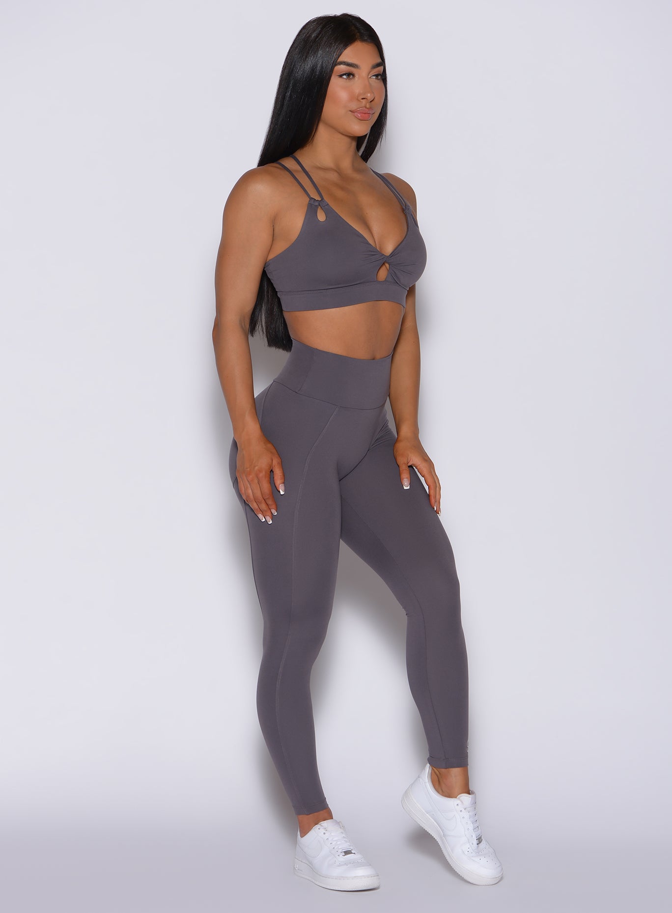 Right side profile view of a model angled slightly to her right wearing our new and enhanced shape leggings in gray smoke color and a matching bra