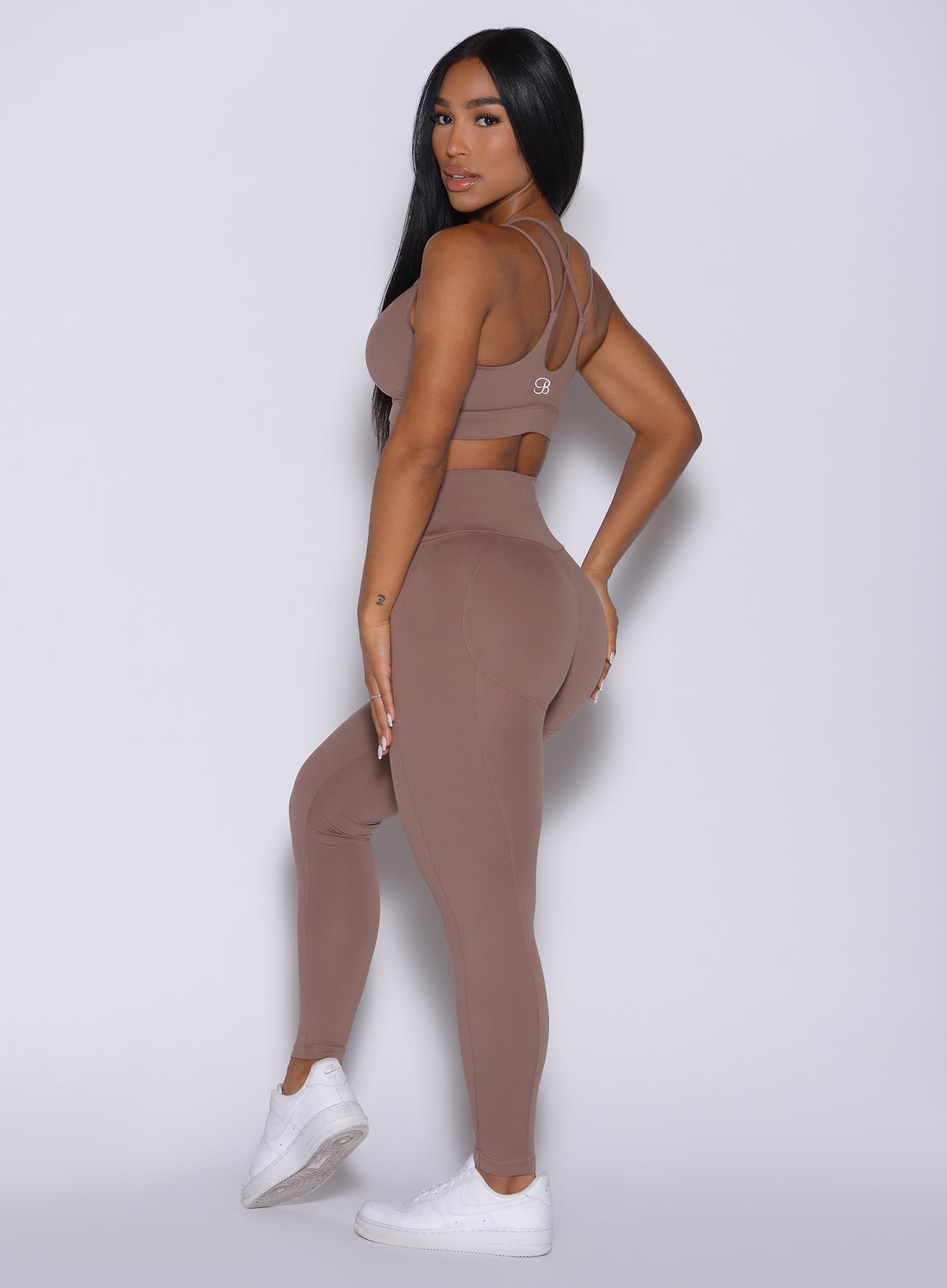 Left side profile view of a model facing to her left wearing our new and enhanced shape leggings in tan color and a matching bra