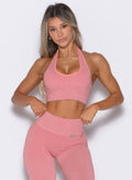front profile view of a model adjusting the waistband of the leggings wearing the Shimmer Backless Bra in Pink star color