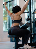 Back profile view of a model working out at the gym wearing the Shimmer V Back Leggings in Black star color