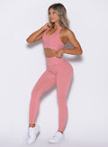 front left side profile view of a model with one hand on the waistband of the leggings and the other on the strap of the bra wearing the Shimmer V Back Leggings in Pink star color