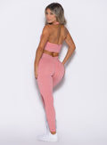 back profile view of a model looking over her shoulder wearing the Shimmer V Back Leggings in Pink star color