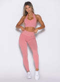 front profile view of a model adjusting the waistband of the leggings wearing the Shimmer V Back Leggings in Pink star color