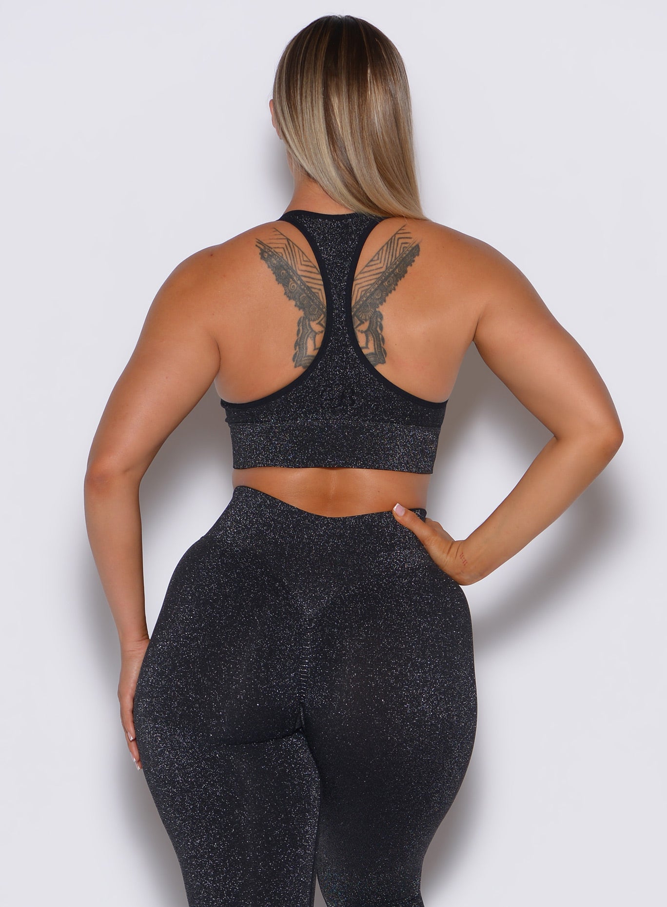 Back profile view of a model wearing our Shimmer Seamless Bra in black sparkle color along with the matching leggings