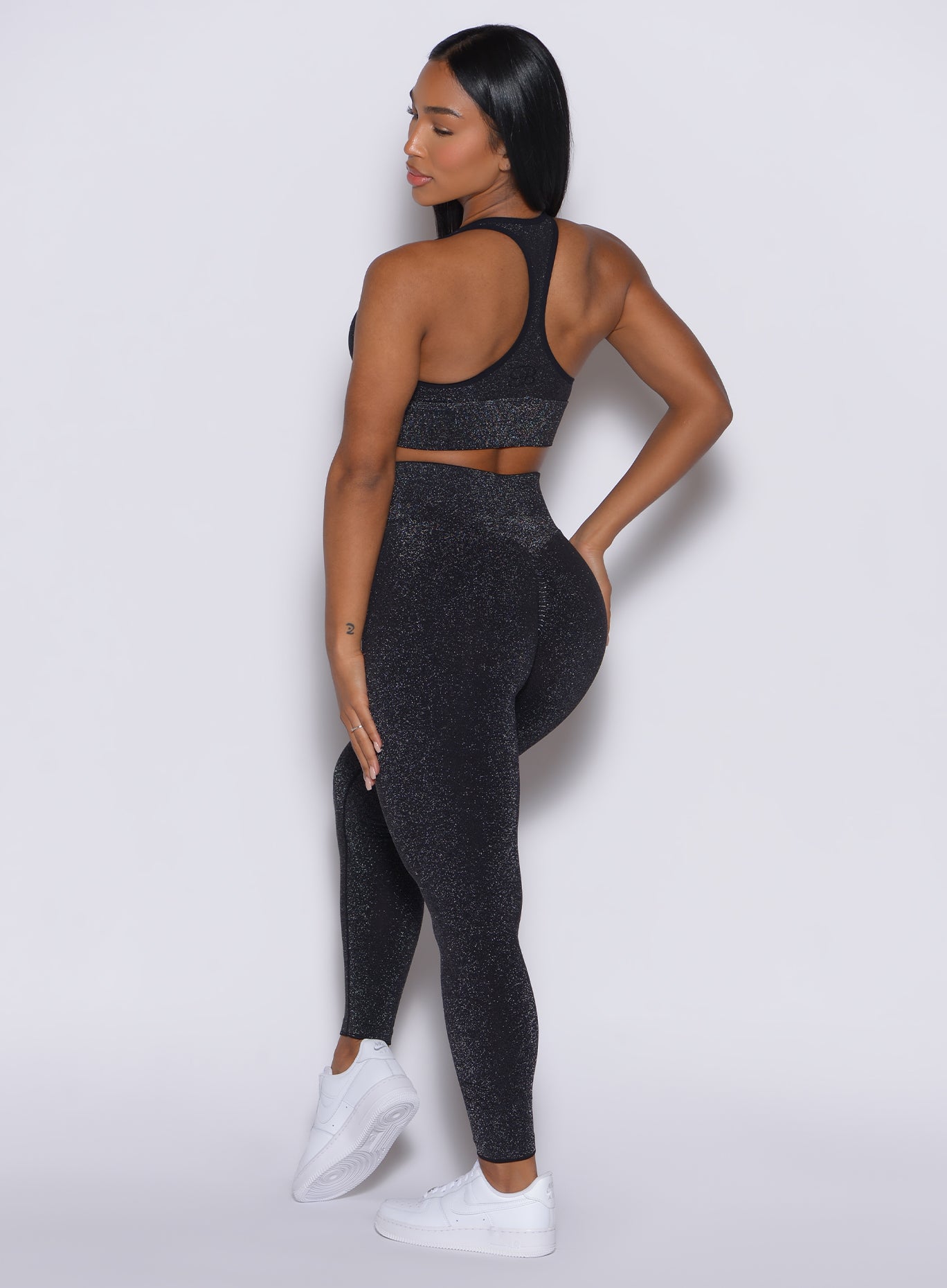 back  side profile view of a model wearing our Shimmer Seamless Leggings in black sparkle color along with the matching shimmer bra