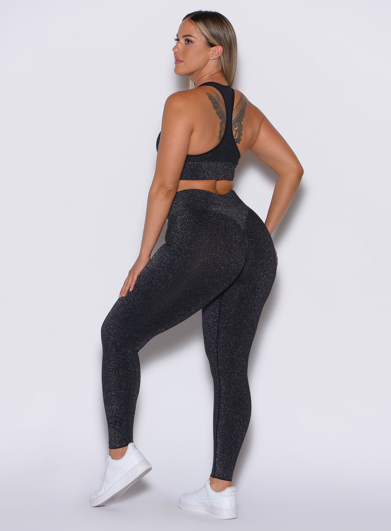 left side profile view of a model facing to her left wearing our Shimmer Seamless Leggings in black sparkle color along with the matching bra