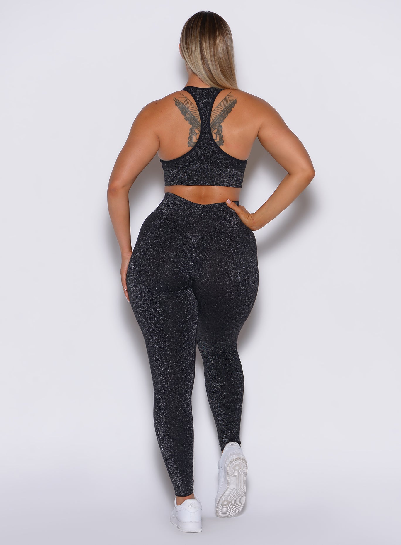 Back profile view of a model wearing our Shimmer Seamless Leggings in black sparkle color along with the matching bra