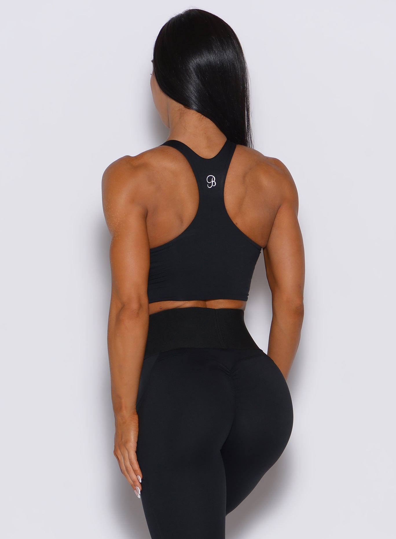Back profile view of a model wearing our black sliced tank bra along with a matching leggings 