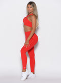 left side view of a model facing to her left wearing our Smooth Leggings and the matching bra in Cherry Bomb color