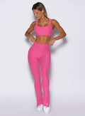 front profile view of a model with both hands holding the waistband wearing the Snape Flare Leggings in pink glo color