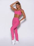 front left side profile view of a model with one hand resting on top of her head wearing the Snape Flare Leggings in pink glo color