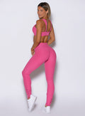 back left side profile view of a model looking over her shoulder wearing the Snape Flare Leggings in pink glo color