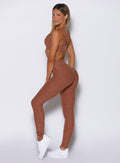 left side profile view of a model looking over her shoulder wearing the Snape Flare Leggings in spiced chai color