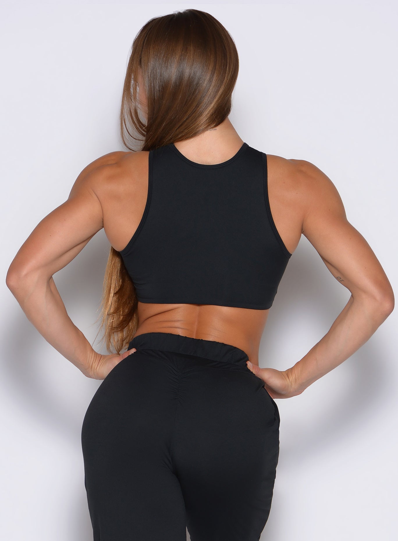 back profile view of a model with both hands on her waist wearing the Society Tank in black color