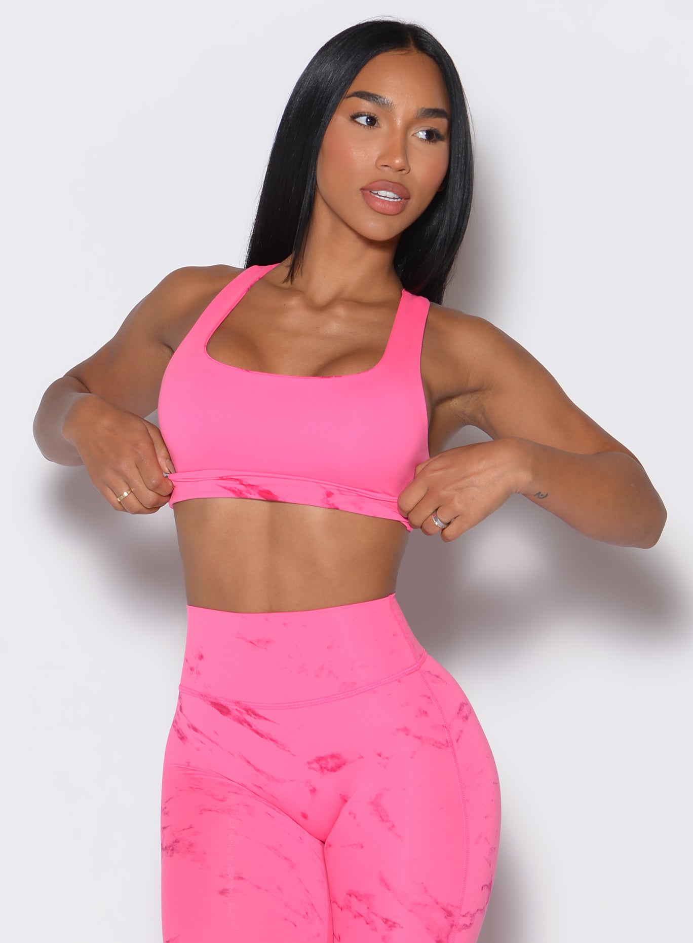 Front profile view of our model holding the bra band and looking to the left wearing our  Square Neck Bra in cotton candy skies color along with the matching leggings