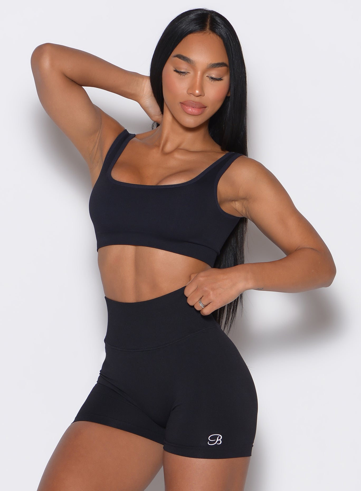 front  profile view of a model holding her hair and wearing our black square neck bra along with the matching shorts