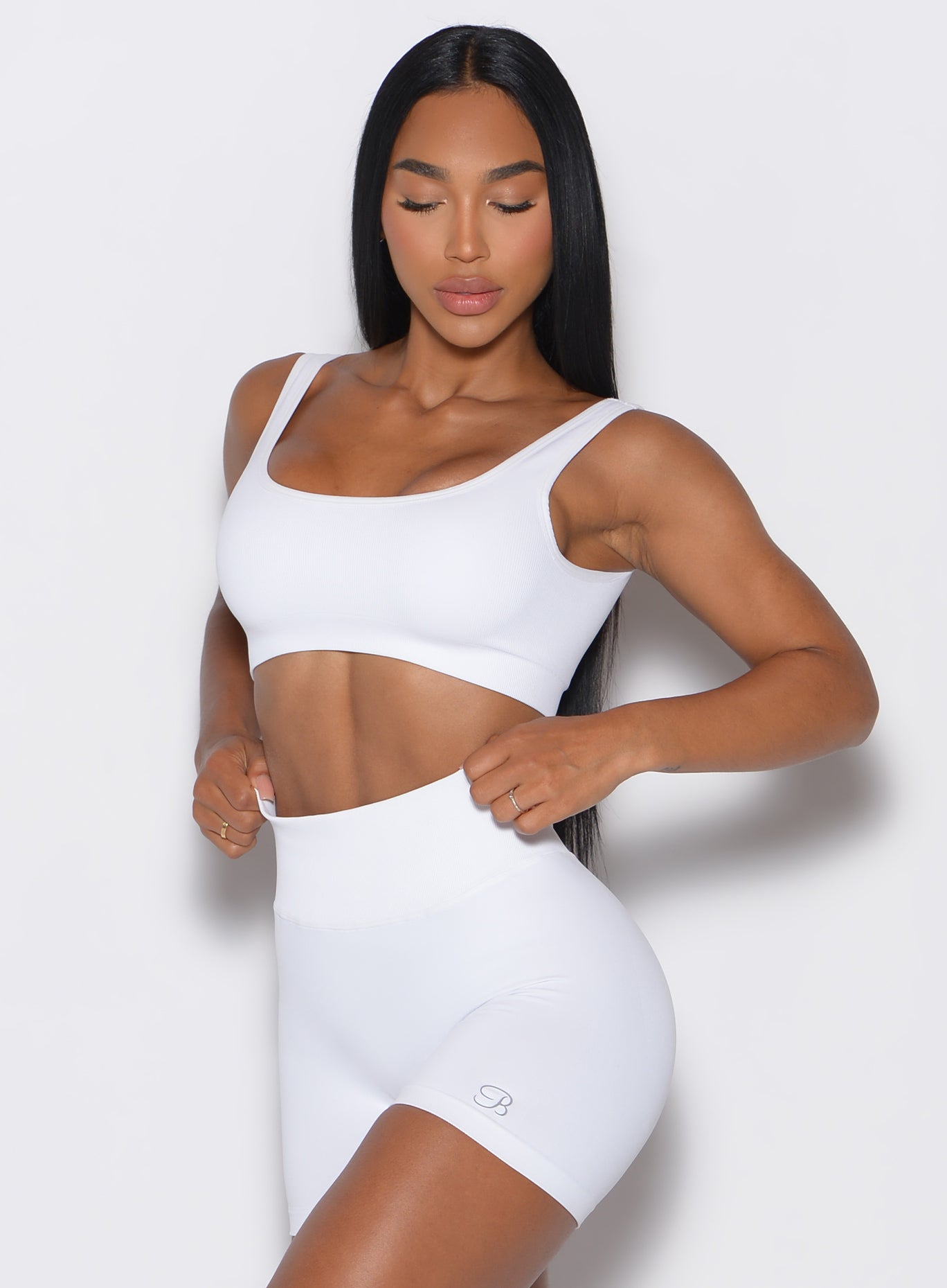 front  profile view of a model adjusting the waistband of her shorts wearing our white square neck bra