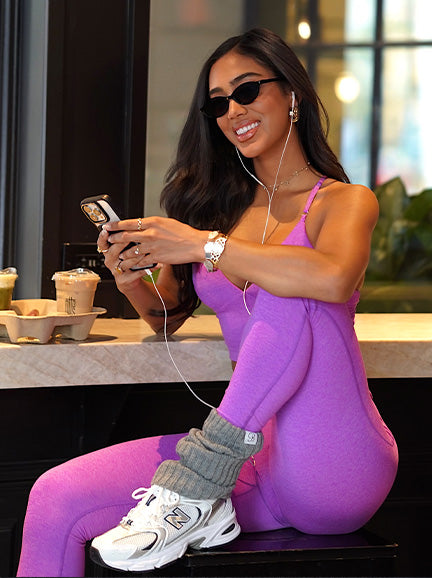 Woman in purple athletic wear sitting on a bench, using a phone with earphones.