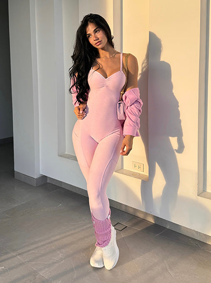 Woman in a pink bodysuit standing against a white wall.