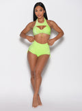 front profile view of a model adjusting the waistband wearing the Sunkissed Sparkle Swim Shorts in Electric Lime color