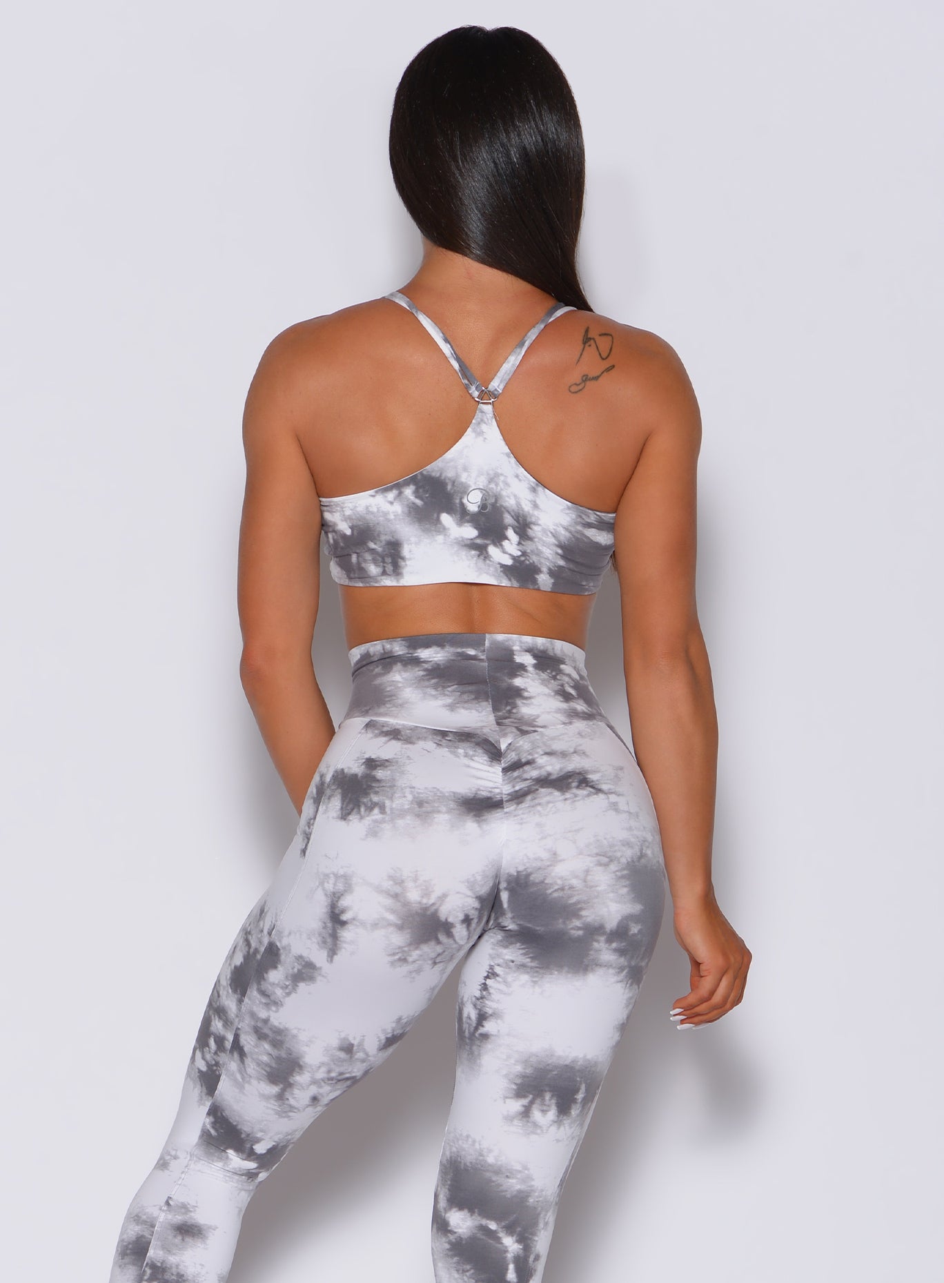 Back  profile view of a model in our topnotch bra in tie dye white gray color and a matching leggings
