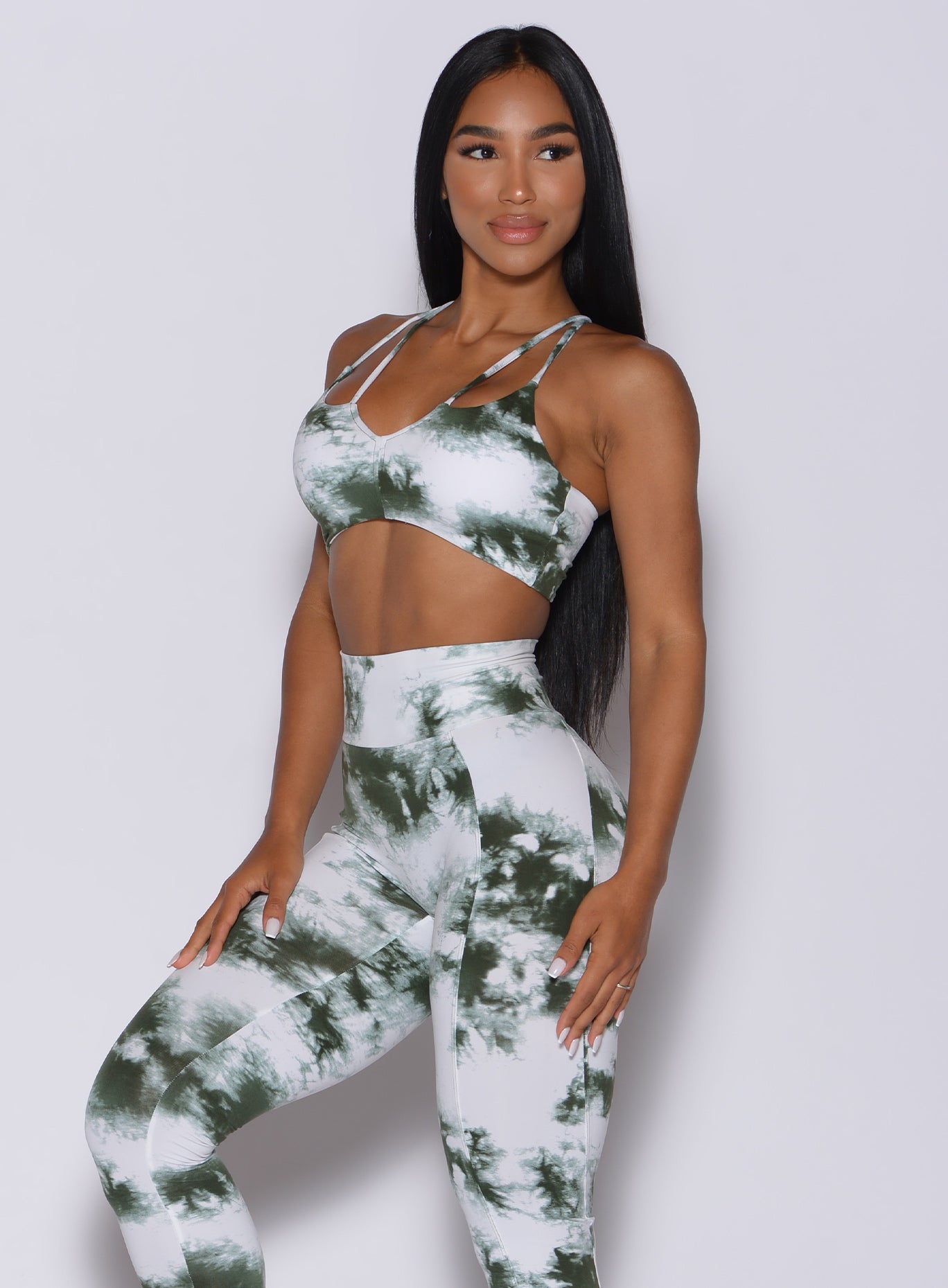 Left side profile view of a beautiful model angled slightly to her left wearing our topnotch bra in tie dye white green color and a matching leggings