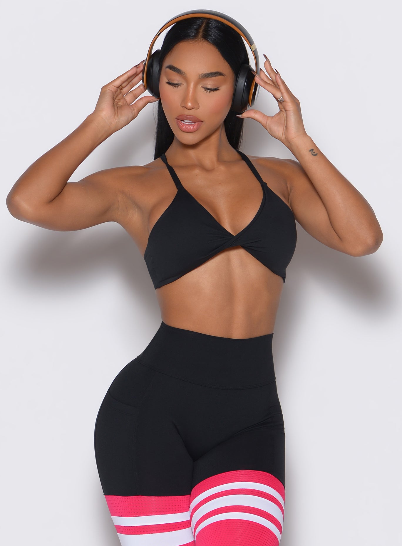 Front profile view of a model adjusting her headphones wearing our black Twist Mini Bra complimented by a matching thigh high