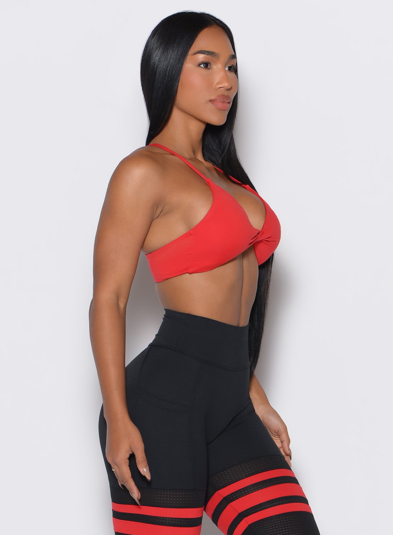 Right side profile view of a model wearing the Twist Mini  Bra in Fire color complemented by a matching thigh high 