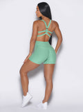 back profile view of a model wearing our tiny waist shorts in sage color along with the matching sports bra